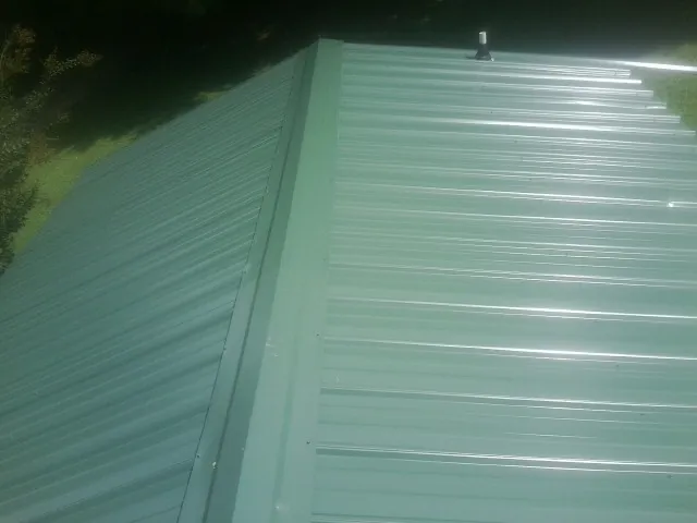 New green metal panels meeting at the ridge of a roof — Flat Roof Repair work by our crew in Wallace